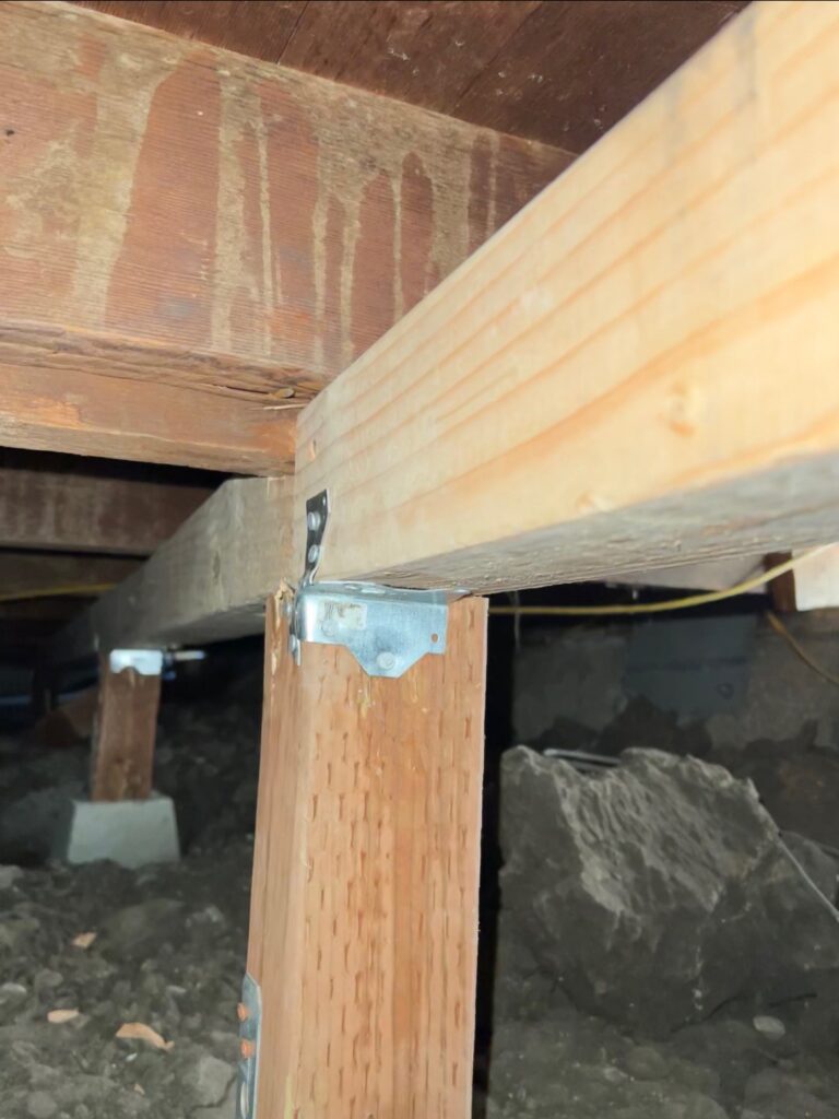 Wooden beams with metal brackets in crawlspace.