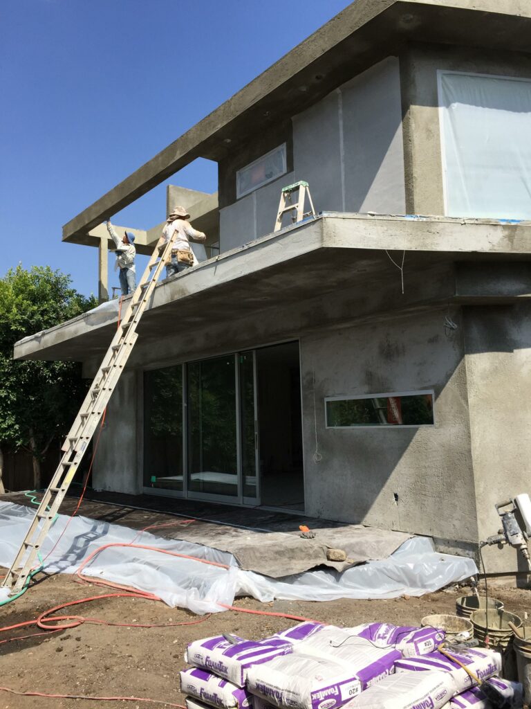 Workers plastering exterior of modern house under construction