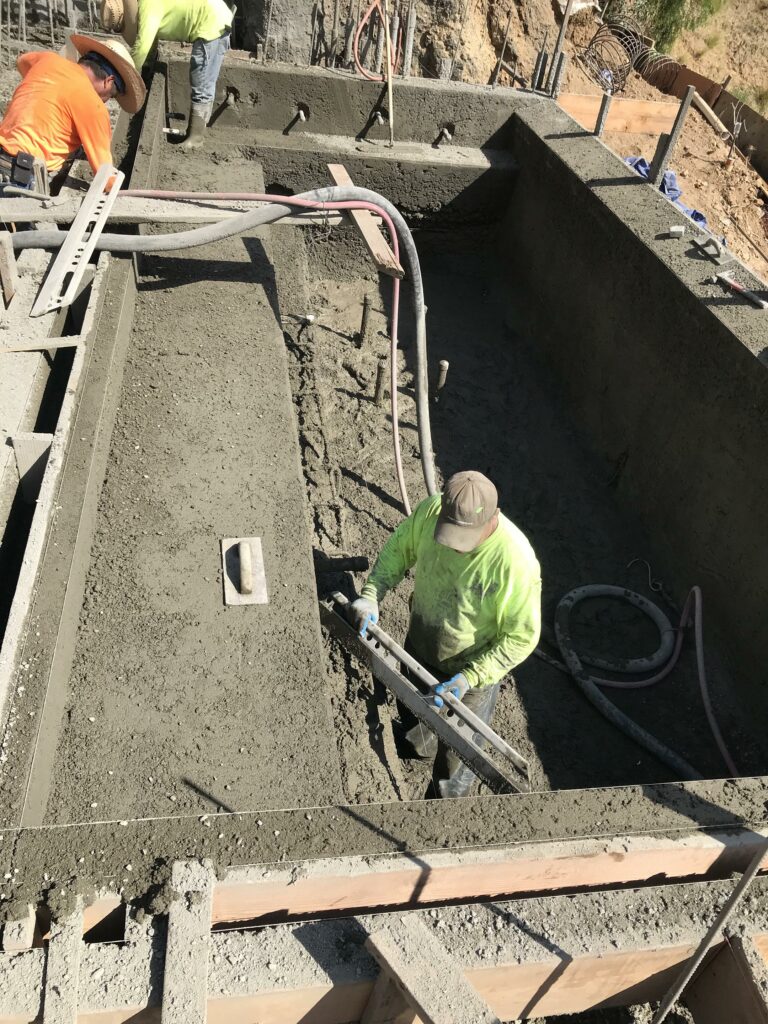 Workers pouring concrete foundation at construction site.