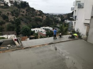 Workers smoothing concrete on rooftop with scenic backdrop.