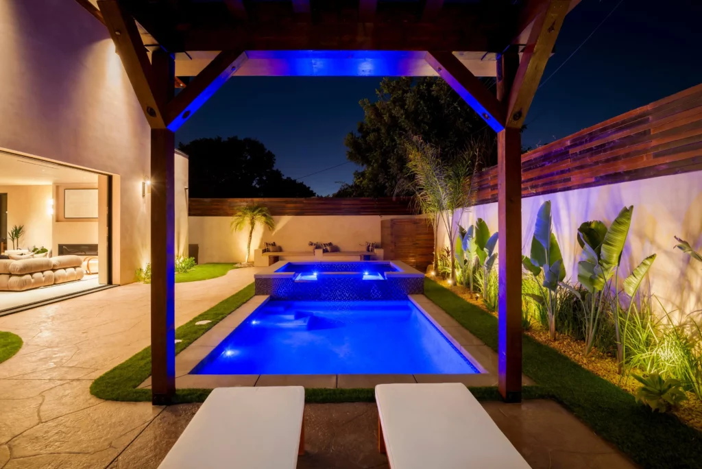 Illuminated backyard pool with loungers at dusk