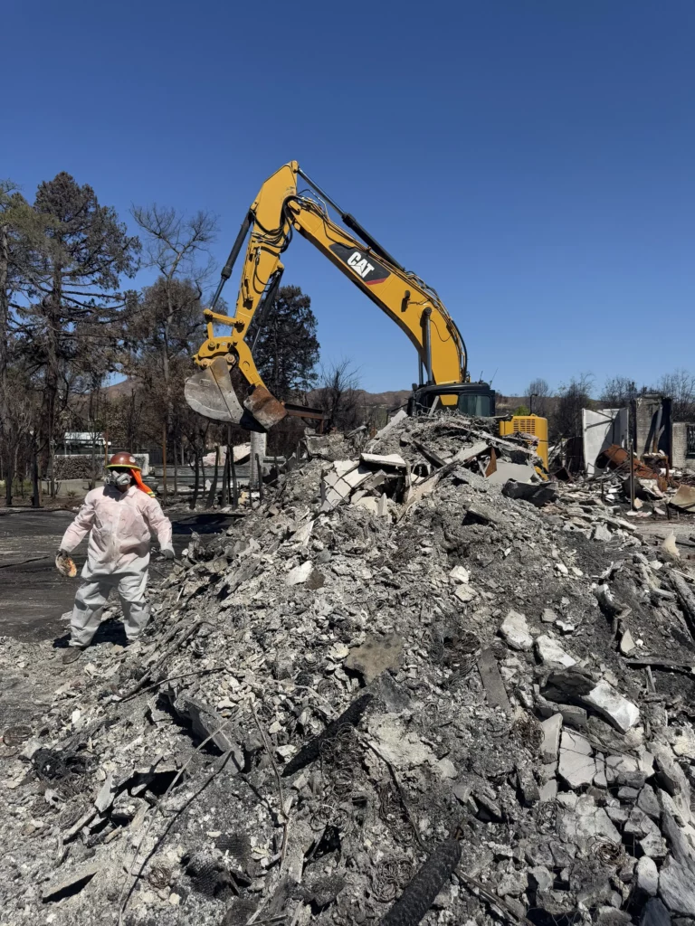 Worker near excavator clearing debris at burnt site